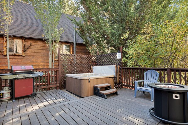 Een houten terras met een jacuzzi, een barbecue en een vuurkuil.