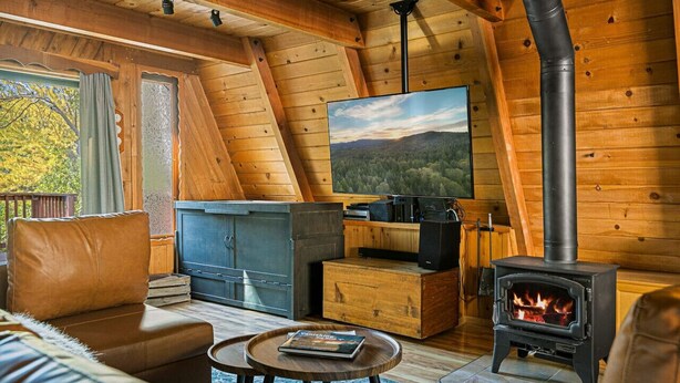Un intérieur de chalet chaleureux avec une grande télévision, un poêle à bois et un canapé.