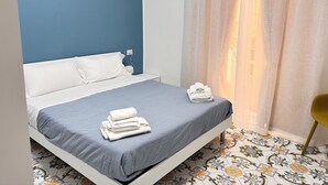 A neatly made bed with a grey bedspread and white pillows, a stack of white towels, and a yellow chair. - La Maison di Partenope (Naples)