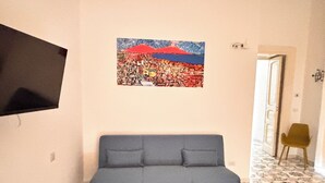 A room with a blue sofa, a wall-mounted TV, and a colorful painting of a cityscape. - La Maison di Partenope (Naples)