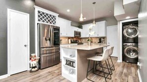 A modern kitchen with stainless steel appliances, a central island with bar stools, and a built-in washing machine. - Beautiful 3-bedroom Patio Home in Houston w/ WiFi, AC near Champions Golf course (Houston)