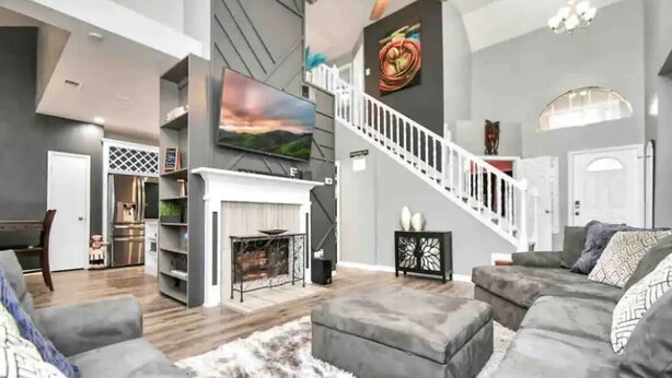 A modern living room with a fireplace, grey sofas, a staircase, and a flat-screen TV. - Beautiful 3-bedroom Patio Home in Houston w/ WiFi, AC near Champions Golf course (Houston)