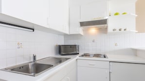 A modern kitchen with white cabinets, a stainless steel sink, a microwave, and a gas stove. - Spacious Apartment With View (Middelkerke)