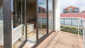 A balcony with a glass door, a white sofa, and a small table. - Spacious Apartment With View (Middelkerke)