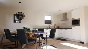 A modern kitchen with white cabinets, a microwave, and a dining area with black chairs and a wooden table. - Chalet in Friesland Near Large Lakes (Sint Nicolaasga)