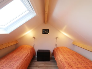 Une petite chambre agréable, dotée de deux lits simples, d’une lucarne et d’une petite table.