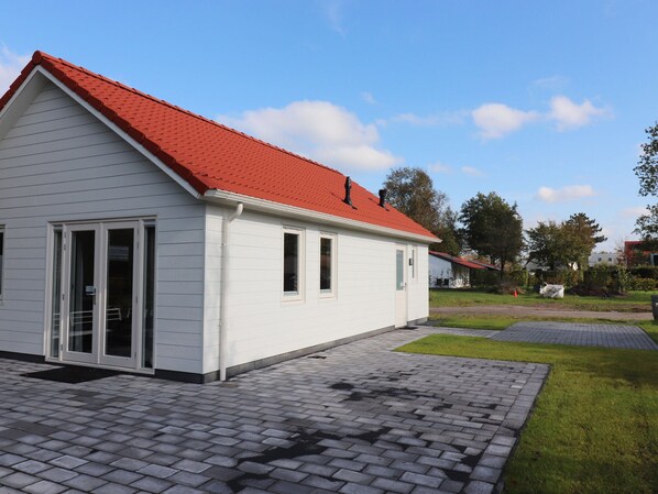 A white building with a red roof, a paved driveway, and a grassy area with trees.