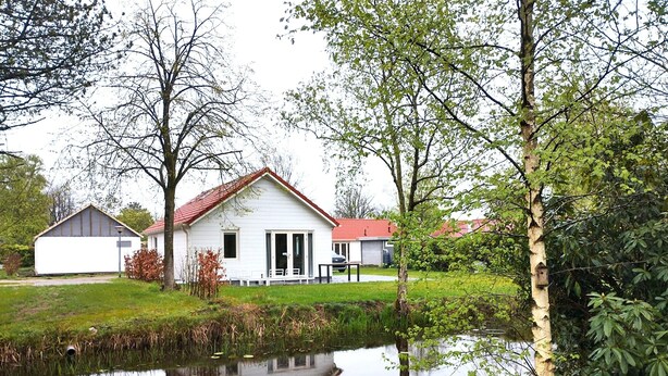 A white house with a red roof, a pond in front, and a small shed to the left. - Chalet in Friesland Near Large Lakes (Sint Nicolaasga)