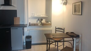 Een kleine keuken met een inbouwvaatwasser, een compacte koelkast en een houten eettafel met twee stoelen.