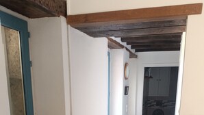 Een hal met een houten plafond, een blauwe deur en een witte muur met een raam.