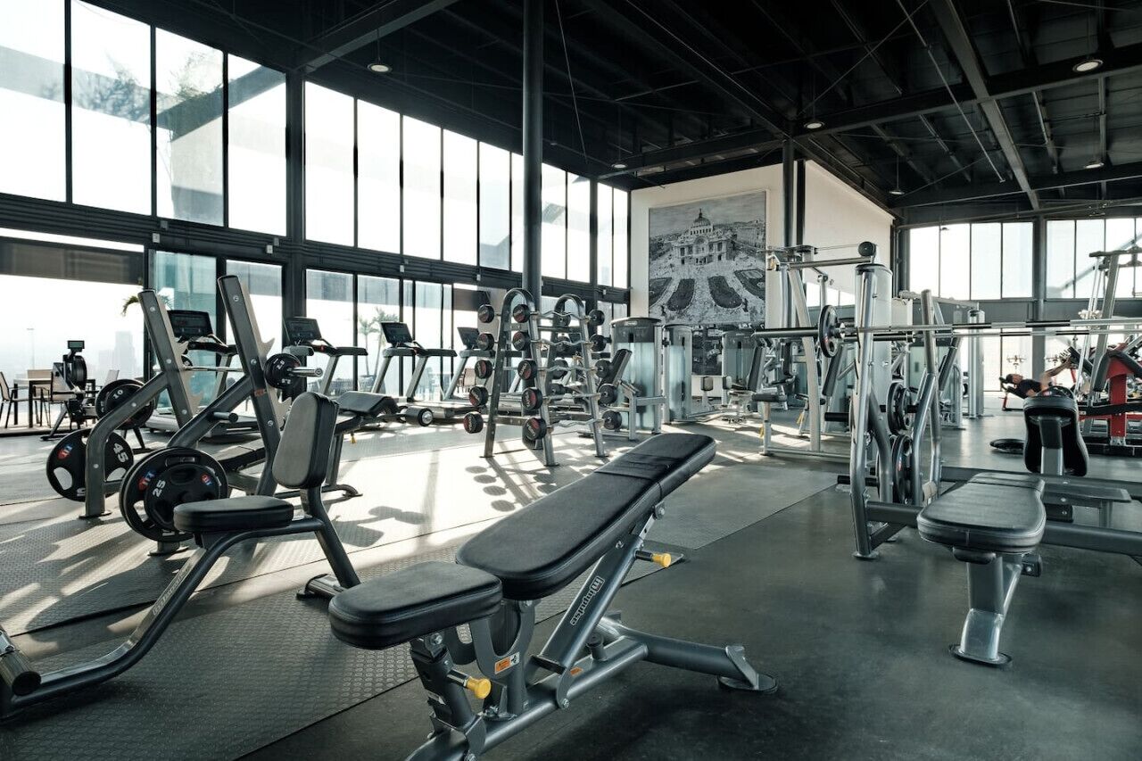 Ein Fitnessstudio mit unterschiedlichen Trainingsgeräten, großen Fenstern und einer Bank.