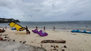 Una playa con gente, barcos y cometas volando.
