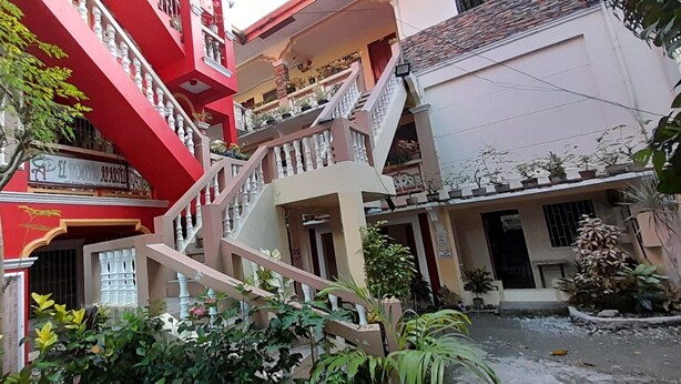 Un edificio de varios pisos con fachada roja, una escalera y balcones con plantas en macetas.