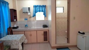 Una cocina compacta con una mesa de comedor, una ventana con cortinas azules, aire acondicionado integrado y un refrigerador pequeño.