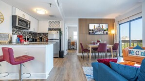 A modern kitchen with white cabinets, a central island, and a dining area with a view. - Lakeview apt 2 suítes 6 min Universal Studios free parking resort no extra fee (Orlando)