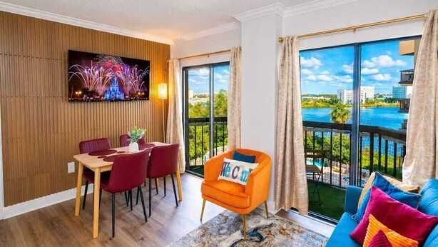 A modern living room with a dining area, a sofa, and a TV displaying fireworks. - Lakeview apt 2 suítes 6 min Universal Studios free parking resort no extra fee (Orlando)