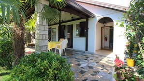 A covered patio area with a stone pillar, a yellow table, and white chairs. - Bungalow mit Schönem Garten und Klimaanlage (Porec)