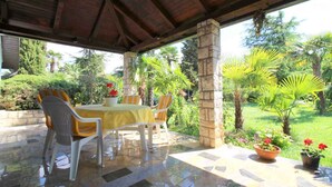 An outdoor patio with a stone-tiled floor, a table with yellow tablecloth, and chairs. - Bungalow mit Schönem Garten und Klimaanlage (Porec)