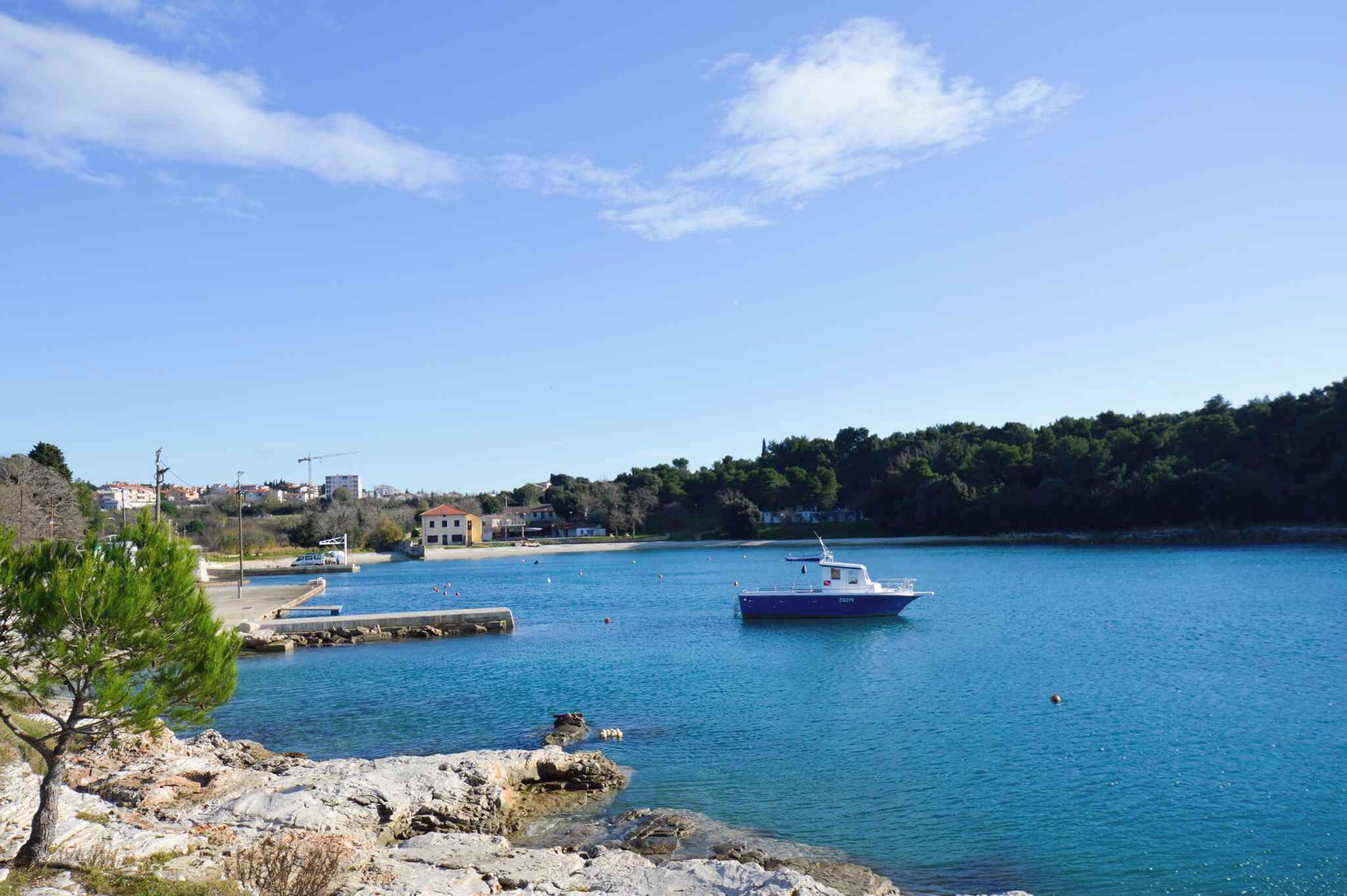 A coastal scene with a boat docked at a pier, calm water, and a rocky shoreline with sparse vegetation.