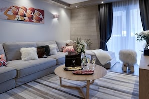A modern living room with a grey sofa, a round coffee table with snacks and drinks, a decorative vase, and a painting on the wall.