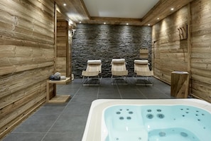 Un cuarto de spa con pared de piedra, paneles de madera, un jacuzzi y tres sillas de mimbre.