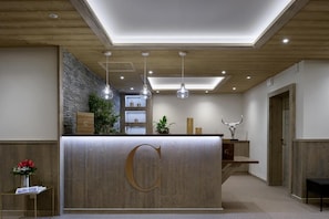 Un espace d’accueil avec un comptoir de réception en bois, un grand logo en forme de « C », des luminaires suspendus, un mur en pierre et une sculpture représentant une tête de taureau.