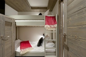 A bunk bed room with a ladder, a red and white blanket, and a white pillow.