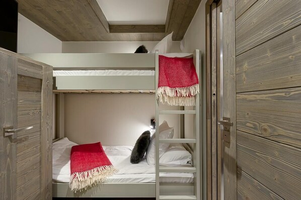 Une chambre avec un lit superposé, une échelle, une couverture rouge et blanche et un oreiller blanc.