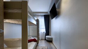Ett litet hotellrum med våningssängar, en liten sittgrupp, en tv och ett fönster med gardiner.