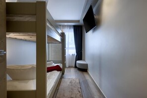 Ein schmales Hotelzimmer mit Etagenbetten, einer kleinen Sitzecke, einem Fernseher und einem Fenster mit Vorhängen.