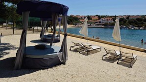 A beachside area with sun loungers and a covered seating area, overlooking a calm sea with buildings in the background. - Ferienwohnung mit Balkon (Medulin)