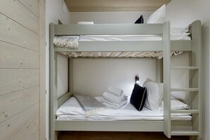 A bunk bed with white bedding, a small shelf, and a ladder.