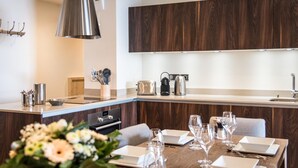 A modern kitchen with dark wood cabinets, stainless steel appliances, and a wooden dining table set for a meal. - Wifi, 200m from resort center, 1st floor, view mountain, sauna, balcony, parking, tv, 91m² (Courchevel)
