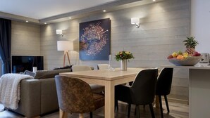 En moderne stue med sofa, spisebord med stole, fjernsyn og vægmonteret lampe.