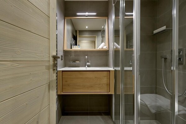 Une salle de bain moderne avec un meuble-lavabo en bois, un miroir, une cabine de douche et une porte en verre.