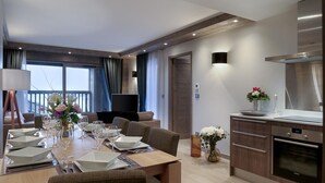 A modern hotel room with a dining area, a TV, a kitchen, and a balcony with curtains. - Wifi, 150m from ski slopes, 2nd floor, view mountain, sauna, balcony, parking, tv, 110m², Courchevel (Courchevel)