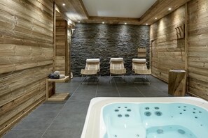 Ein Spa-Raum mit Steinwand, Holzvertäfelung, einer Whirlwanne und drei Korbstühlen.