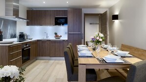 A modern kitchen with wooden cabinets, a built-in oven, and a dining area with a wooden table set for four. - Wifi, 150m from ski slopes, 2nd floor, view mountain, sauna, balcony, parking, tv, 110m², Courchevel (Courchevel)