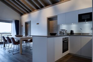 Une cuisine moderne avec des meubles blancs, un four encastré et une grande fenêtre donnant sur un balcon.