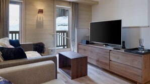 Moderni olohuone, jossa on sohva, sohvapöytä, televisio ja puinen kaappi. Parvekkeelta avautuu näkymä lumipeitteiselle maastolle.