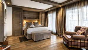 Een slaapkamer met een groot bed, een stoel, houten vloeren en een raam met gordijnen.