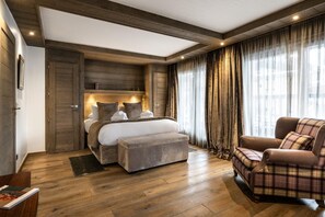 Ein Schlafzimmer mit einem großen Bett, einem Sessel, Holzboden und einem Fenster mit Vorhängen.