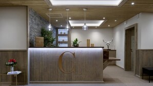 Een receptiegedeelte met een houten receptiebalie, een groot 'C'-logo, hangende verlichting, een stenen muur en een sculptuur van een stierhoofd.
