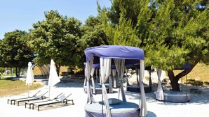 Outdoor seating areas with cushioned benches and umbrellas, surrounded by trees. - Apartments Pjescana Uvala/istrien 11166 (Medulin)