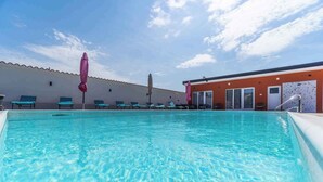 A swimming pool with lounge chairs and umbrellas, a building with a tiled roof, and a clear sky. - Apartments in Pula/istrien 11169 (Pula)