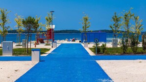 A blue pathway leading to a beach area with a lifeguard tower, beach chairs, and a clear view of the sea. - Apartments in Pula/istrien 11169 (Pula)
