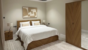Un dormitorio con una cama grande, un armario de madera, una mesita de noche con una lámpara y una obra de arte abstracta colgada en la pared.