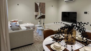 Una sala de estar moderna con un sofá, una mesa de comedor preparada para cuatro personas, un televisor de pantalla plana y un equipo de aire acondicionado en la pared.