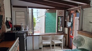 A compact kitchen with a gas stove, a blender, and a refrigerator. There is a dining area with a chair and a table. - Budget Adventurer's Hut (Bridgetown)