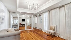 A spacious room with a wooden floor, a sofa, a chair, and a large mirror reflecting the room.